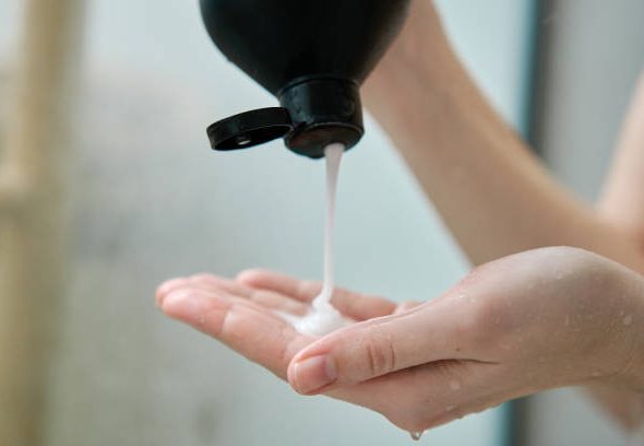 Pouring shampoo from bottle on female hand in bathroom. Hygiene concept