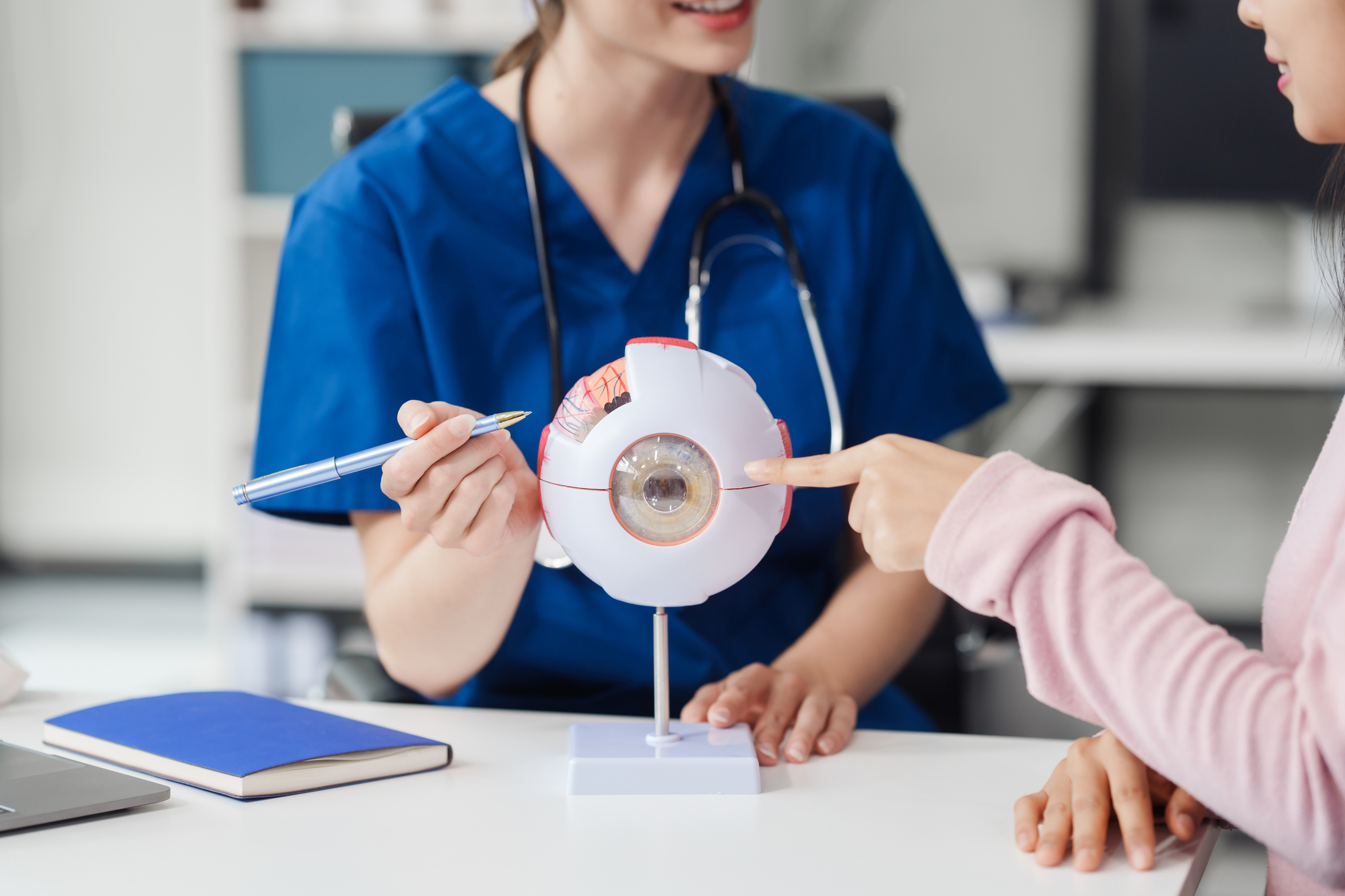 Female Caucasian ophthalmologist explains about eye diseases using the eye model with an Asian female patient At the table in the hospital examination room, Glaucoma, Cataract, Diabetic Retinopathy